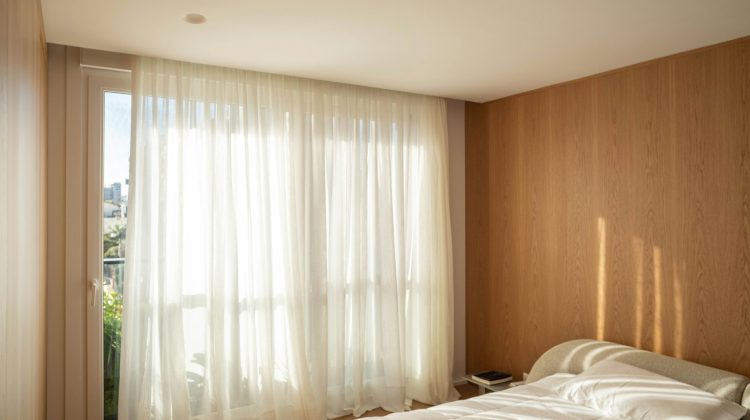A bright bedroom with sheer curtains and sunlight.