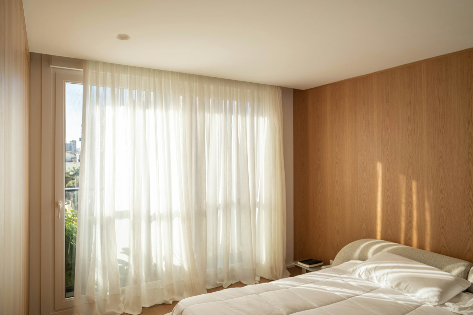 A bright bedroom with sheer curtains and sunlight.