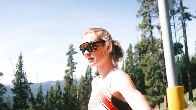 Woman pauses near a ski lift on a sunny day.