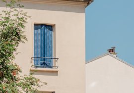 A building's corner with blue shutters and chimney.