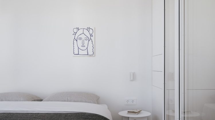 Minimalist bedroom features a bed, art, and a small table.