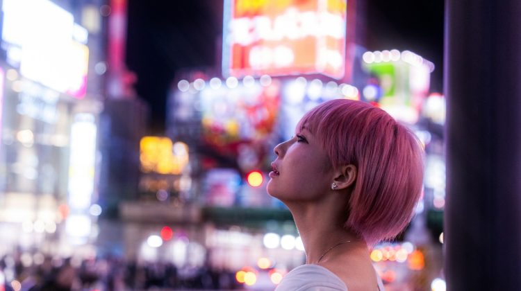 Woman gazes at bright neon signs in the city.